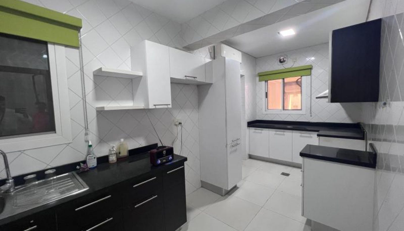 Modern kitchen with black and white cabinets, white tiled walls and floor, two windows with green blinds, and a stainless steel sink.
