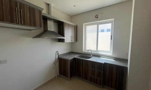 Modern kitchen interior in an AL Hidd rental property, featuring wooden cabinets, stainless steel sink, and a window allowing natural light.