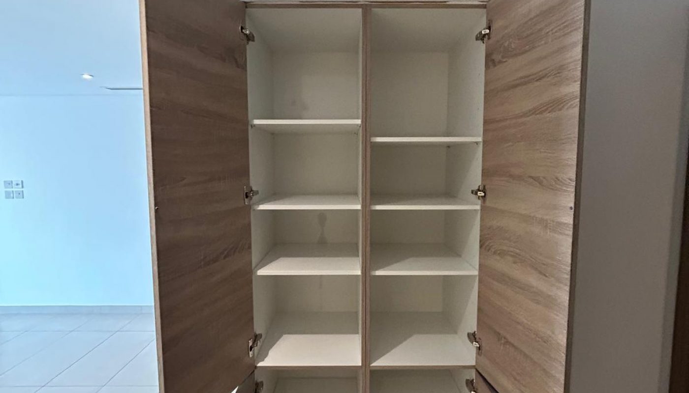 A wooden cabinet with four doors is open, showing multiple empty white shelves inside, positioned against a tiled wall.