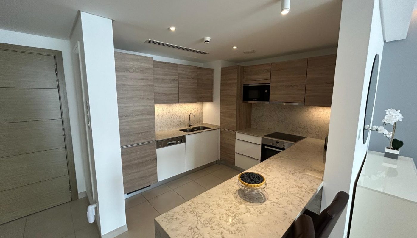 Modern kitchen with wood cabinets, built-in appliances, marble countertop, and bar seating. A decorative bowl and an orchid are placed on the counter and sideboard.