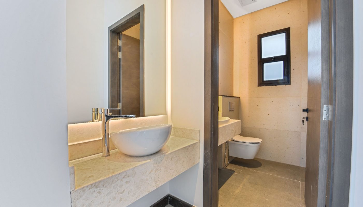 Modern bathroom with a round vessel sink on a marble countertop, large mirror, and a separate toilet area with a small window and beige tiles.