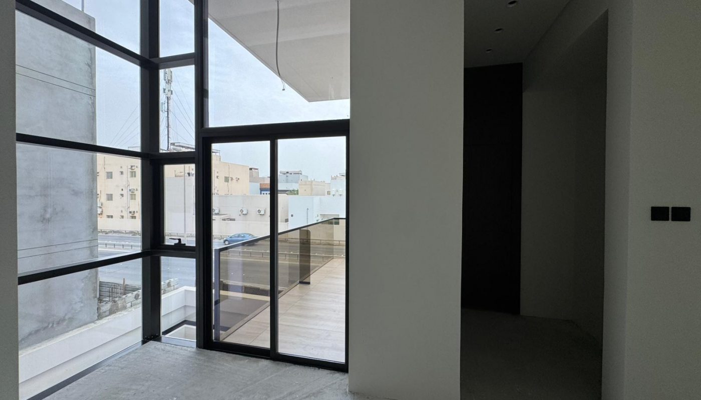 A modern room with large floor-to-ceiling windows, a glass door leading to a balcony, and unfinished concrete flooring.