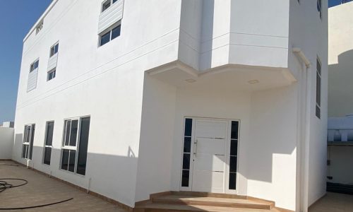 Modern white building with a flat roof, central entrance door, and multiple windows under a clear blue sky. Auto Draft