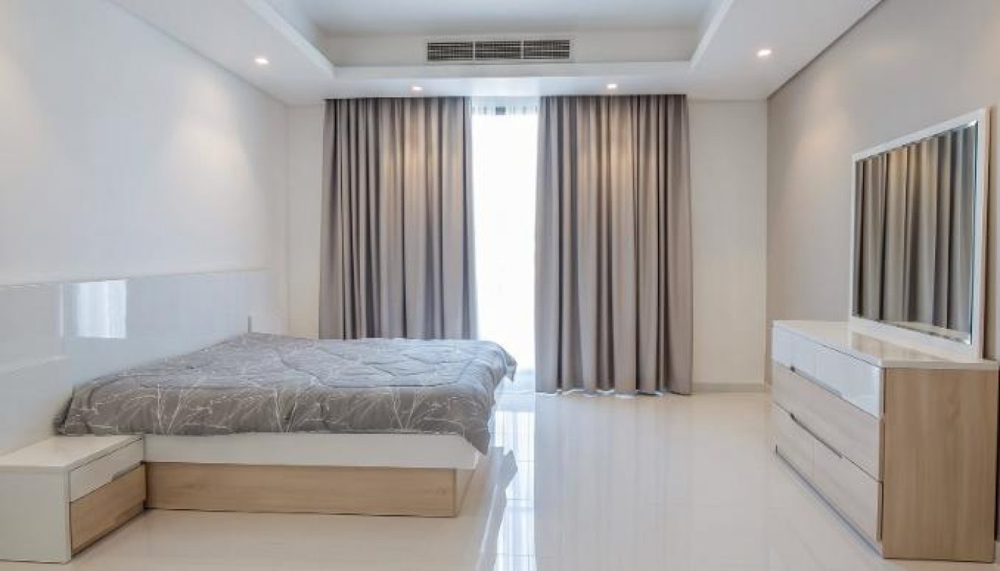 Minimalist bedroom with a double bed, bedside table, dresser, large mirror, and floor-to-ceiling curtains covering a window.