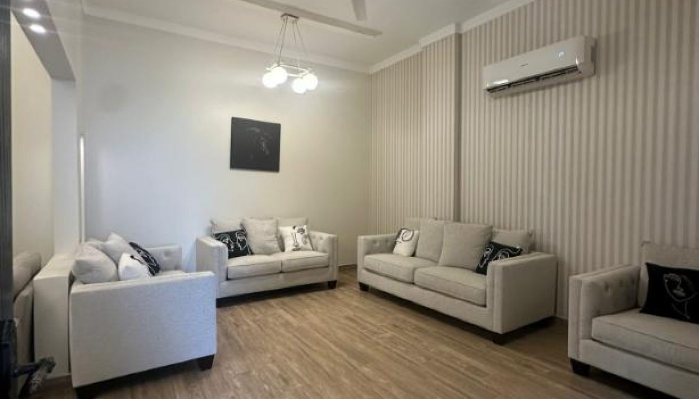 A modern living room with three beige sofas, wood-patterned flooring, striped accent wall, ceiling lights, a ceiling fan, and a wall-mounted air conditioner.