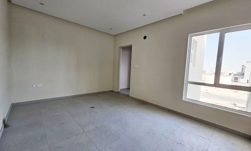 An empty room with beige walls, a tile floor, and a window showing a city view in a luxurious villa.