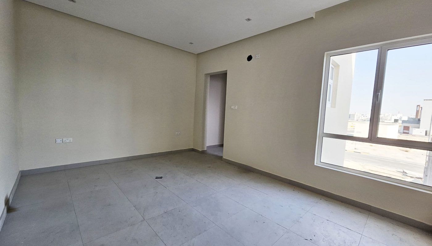 An empty room with beige walls, a tile floor, and a window showing a city view in a luxurious villa.