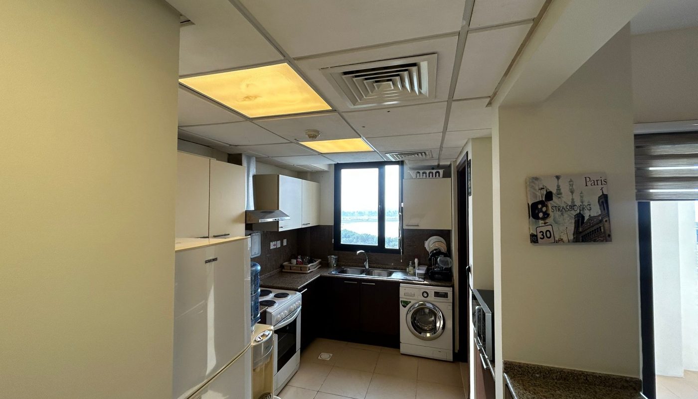 Modern kitchen with white and brown cabinets, appliances including a washing machine and oven, a window with outdoor view, and a wall decor piece.