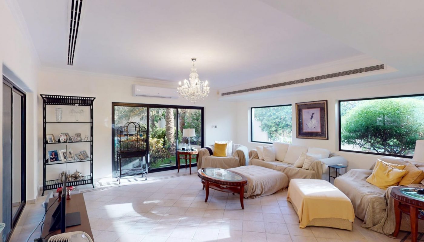 Spacious living room with light-colored sofas, glass coffee tables, large windows, sliding glass door, chandelier, and tiled floor.