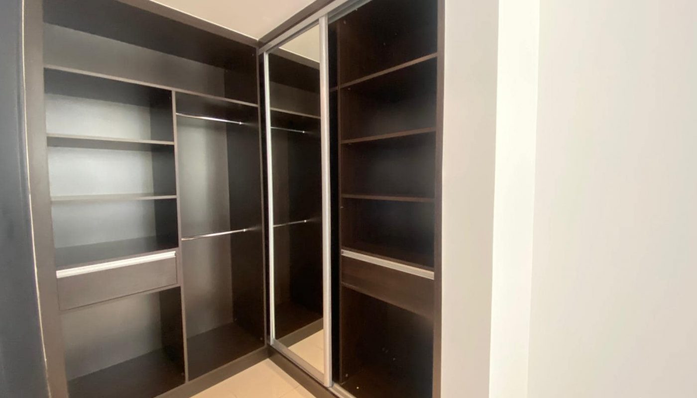 Walk-in closet with dark wood shelves and drawers, sliding glass doors on the right side, and a light tiled floor.