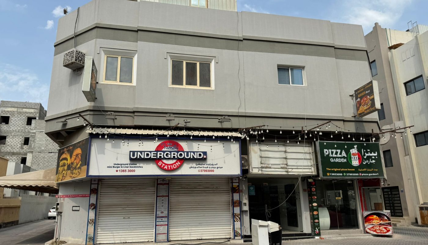 A two-story gray building with closed shops on the ground floor, including "Underground Station" and "Pizza Garden," located on a quiet street.