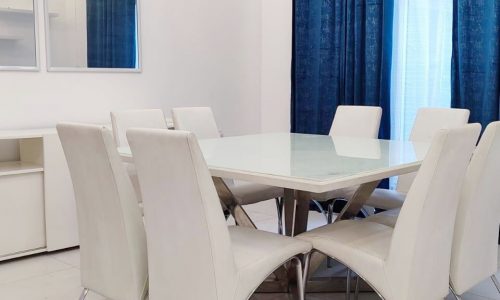 A fully furnished modern dining room featuring a white table with matching chairs and blue curtains.