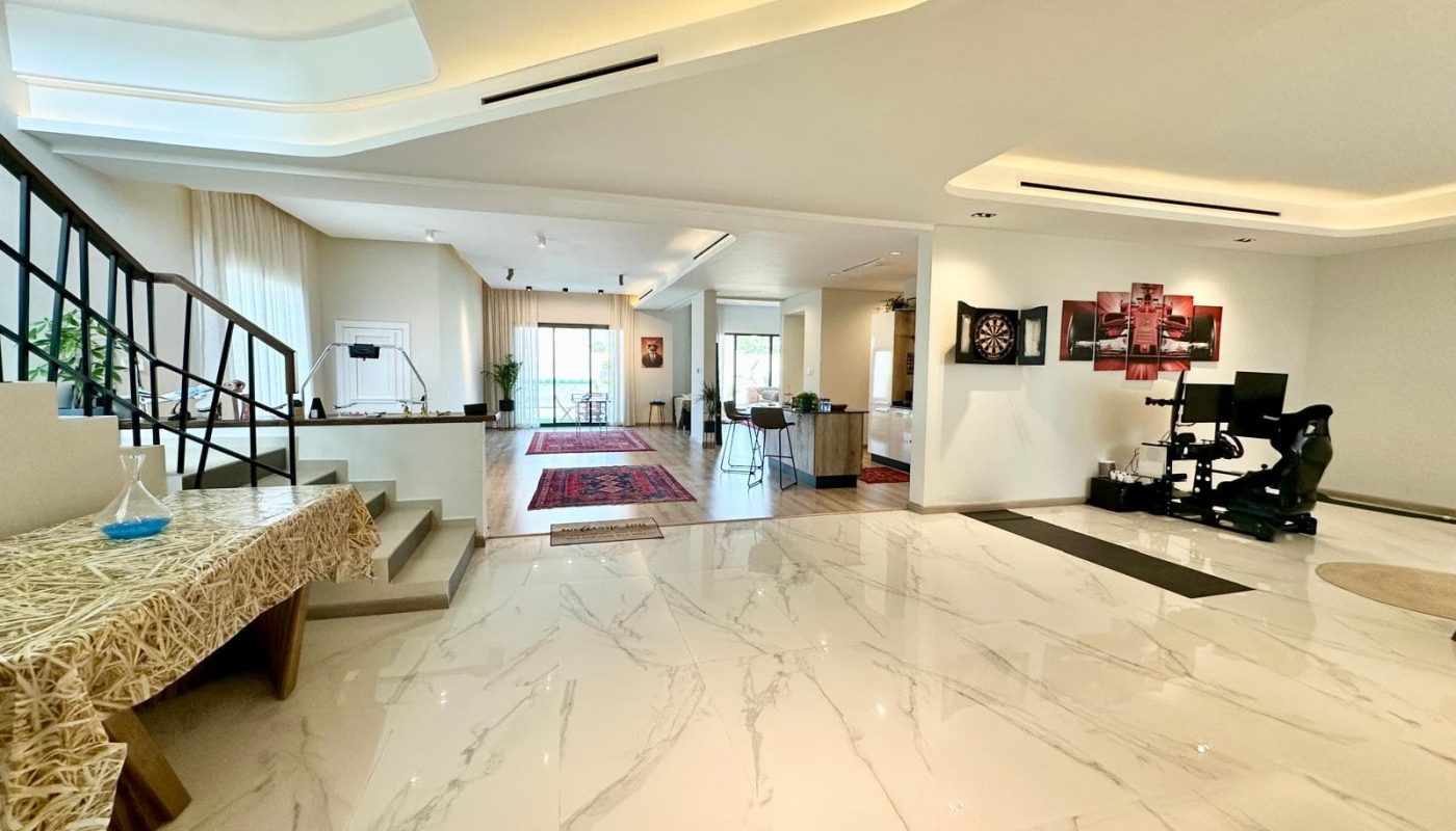 Spacious, modern open-plan living area with marble floors, a staircase, gaming setup, dining area, large windows, and contemporary decor.