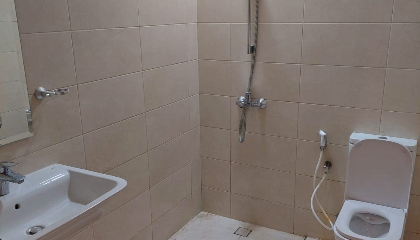 Bathroom with beige tiles, featuring a sink, a mounted mirror, a shower head, and a toilet.