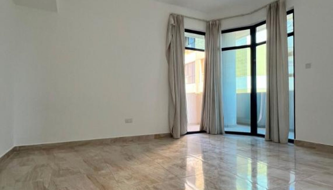 Empty room with marble tile floor, white walls, ceiling light, and large windows with beige curtains leading to a small balcony.