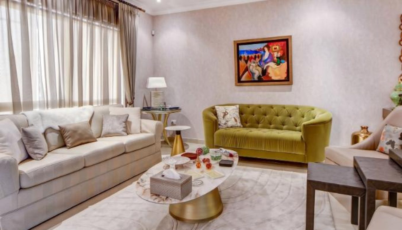 A modern living room with a beige sofa, green couch, marble coffee table, wall art, and large windows with curtains.