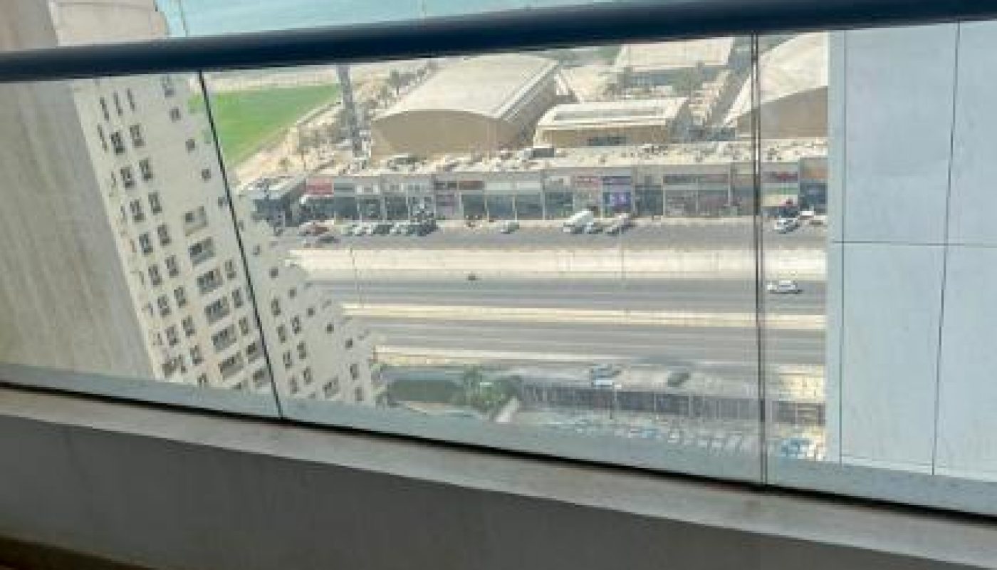 View from a balcony showing a street, buildings, and the sea in the background under a clear sky.