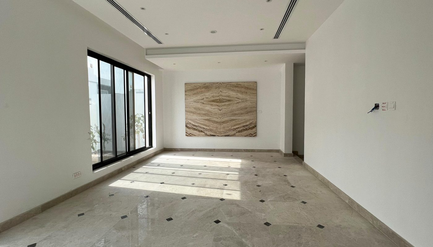 Spacious, empty room with marble floor, large window letting in sunlight, white walls, recessed lighting, and a large decorative panel on the far wall.