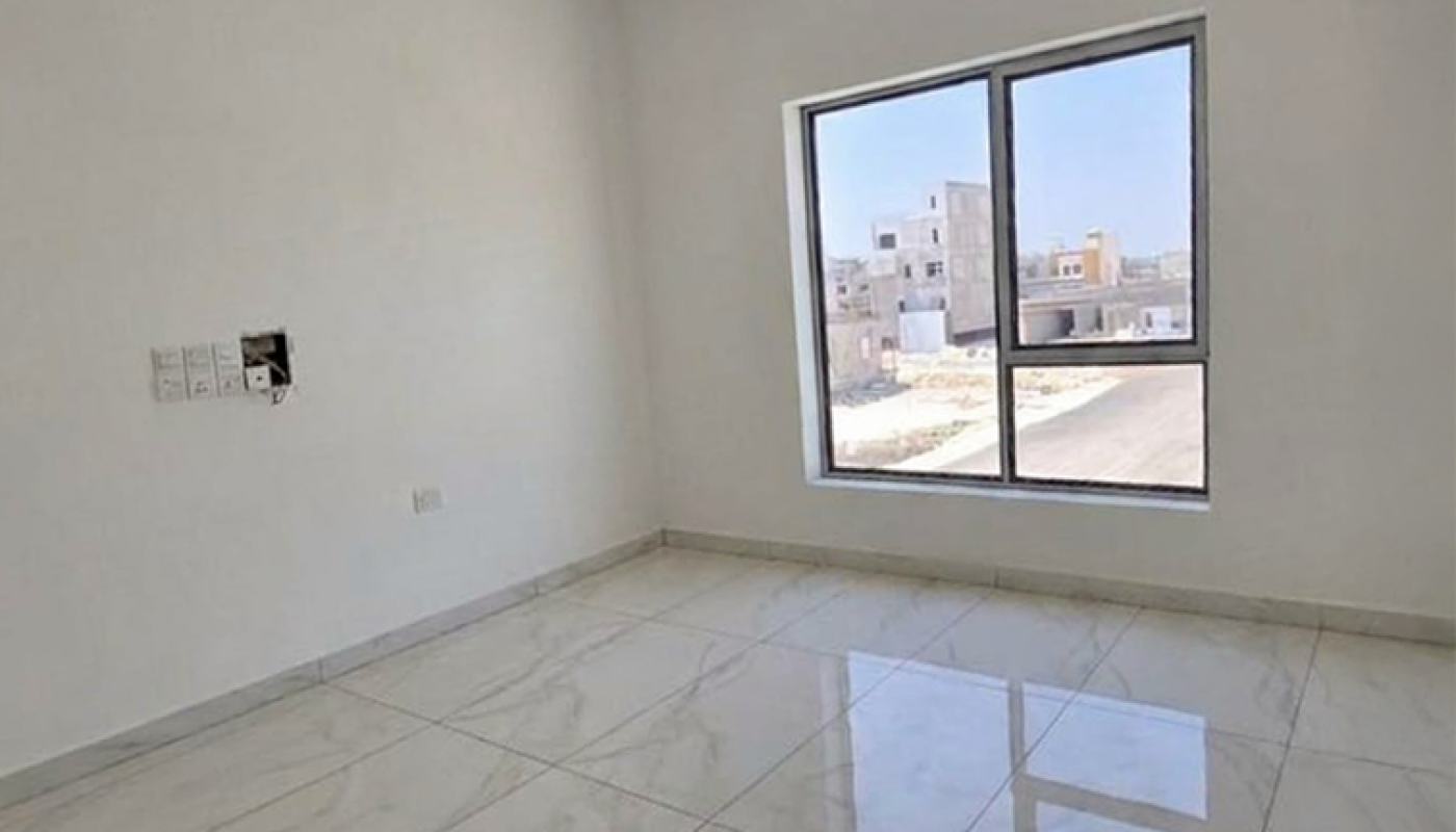 Empty, unfurnished room with white walls, large window, and glossy white marble floor tiles. Daylight streams in through the window, showing buildings outside.