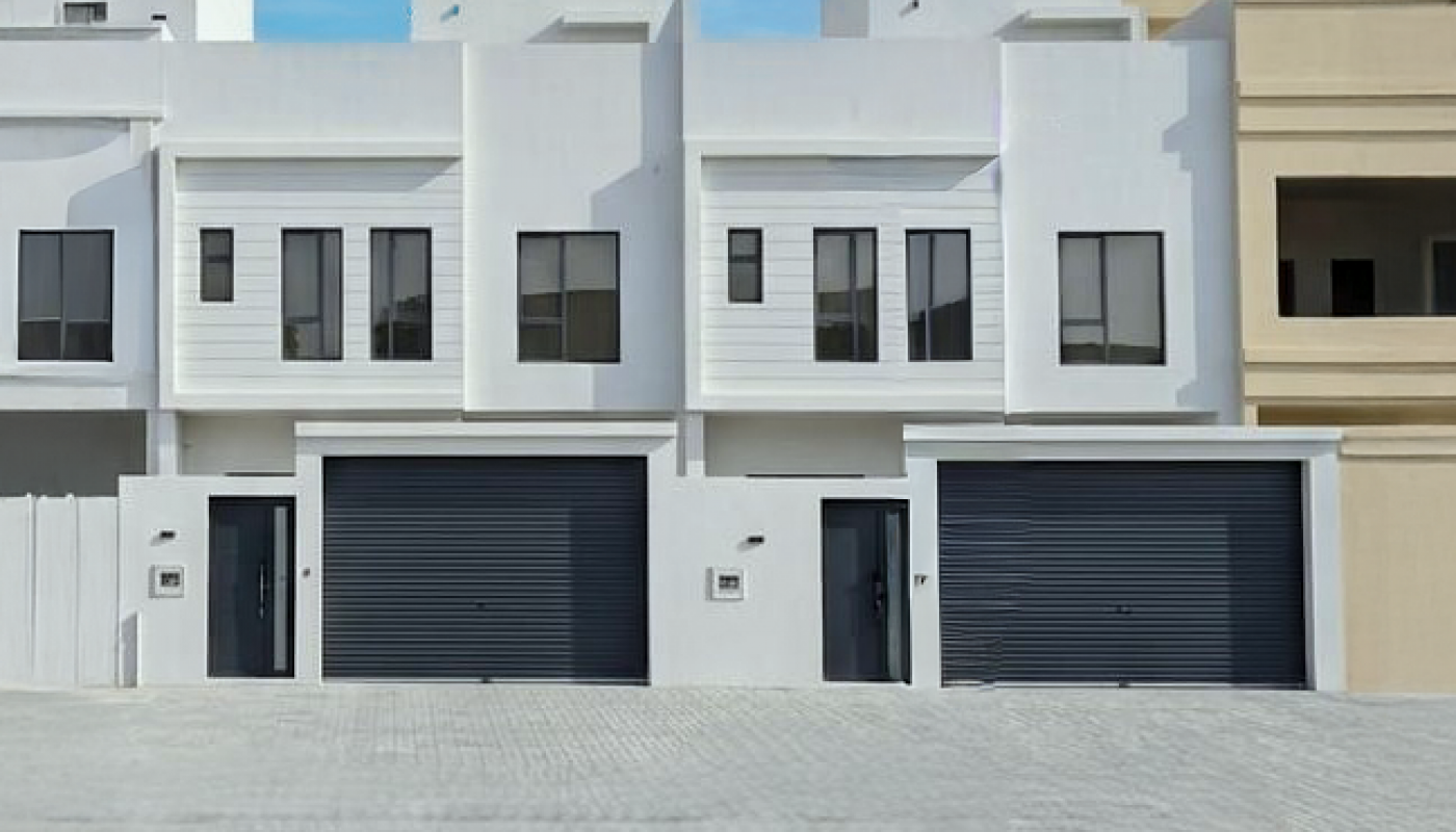A row of modern white townhouses with black garage doors and rectangular windows under a clear blue sky.