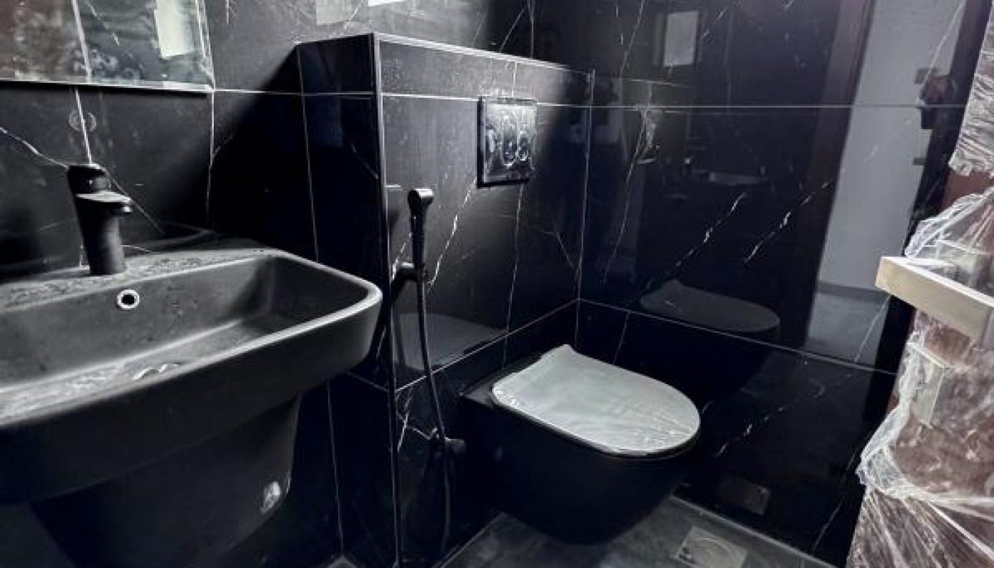 Small modern bathroom with black marble tiles, wall-mounted sink and toilet, a bidet spray, and a window letting in natural light.