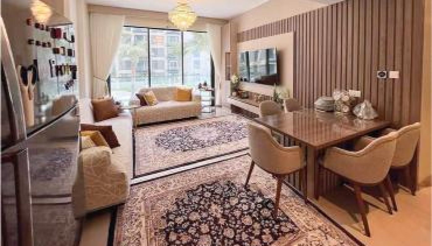 Modern living and dining area with large rugs, beige sofas, dining table with six chairs, wall-mounted TV, and floor-to-ceiling windows with sheer curtains.