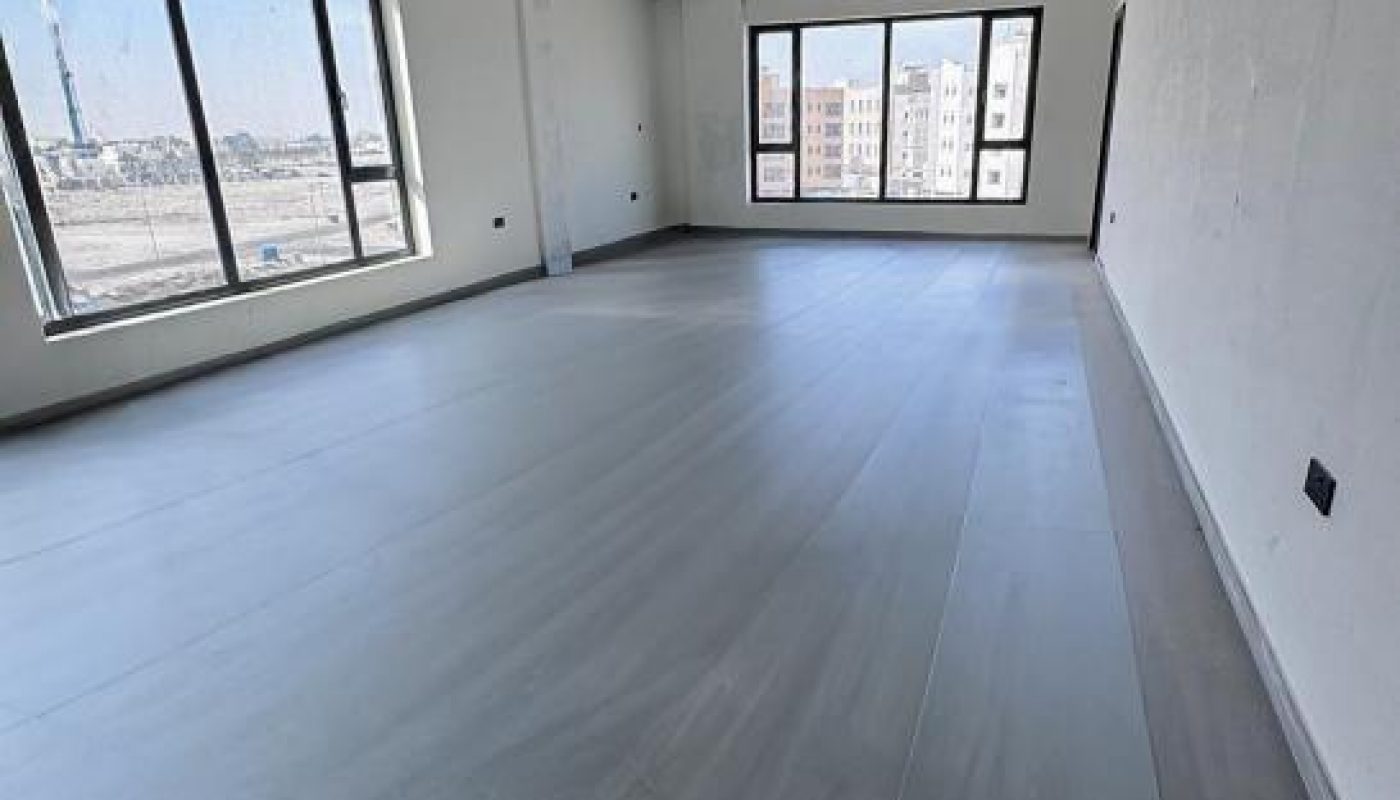 An empty, unfinished room with large windows, concrete ceiling, and tiled floors, overlooking a cityscape.