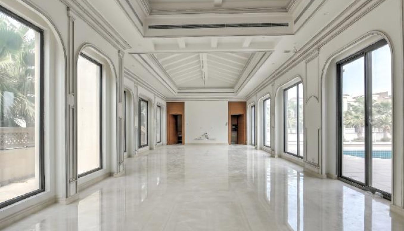 A spacious, empty room with high vaulted ceilings, large arched windows, and polished marble floors, allowing natural light to fill the space.