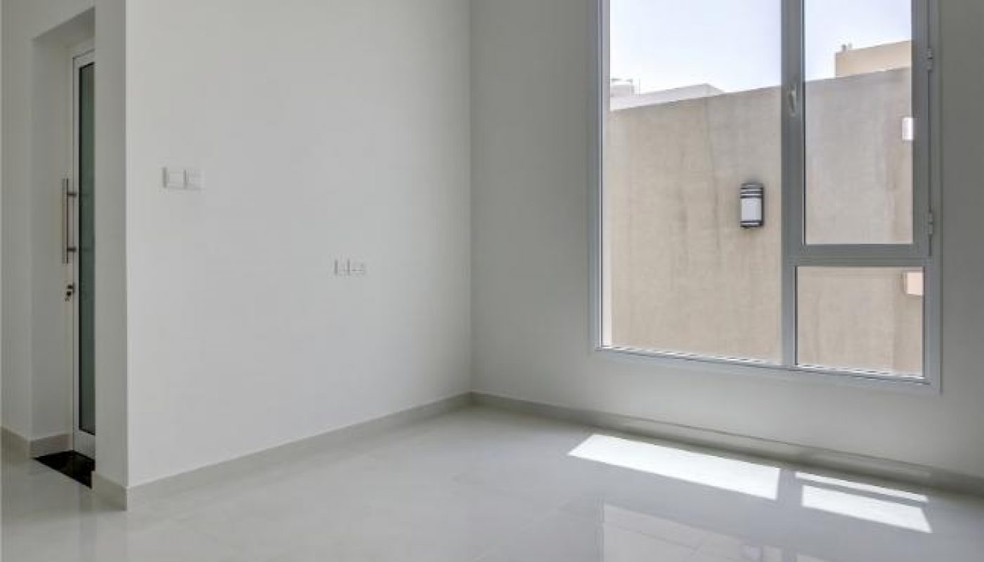 Empty, modern room with white walls, large window letting in natural light, glossy tiled floor, and recessed ceiling lights.