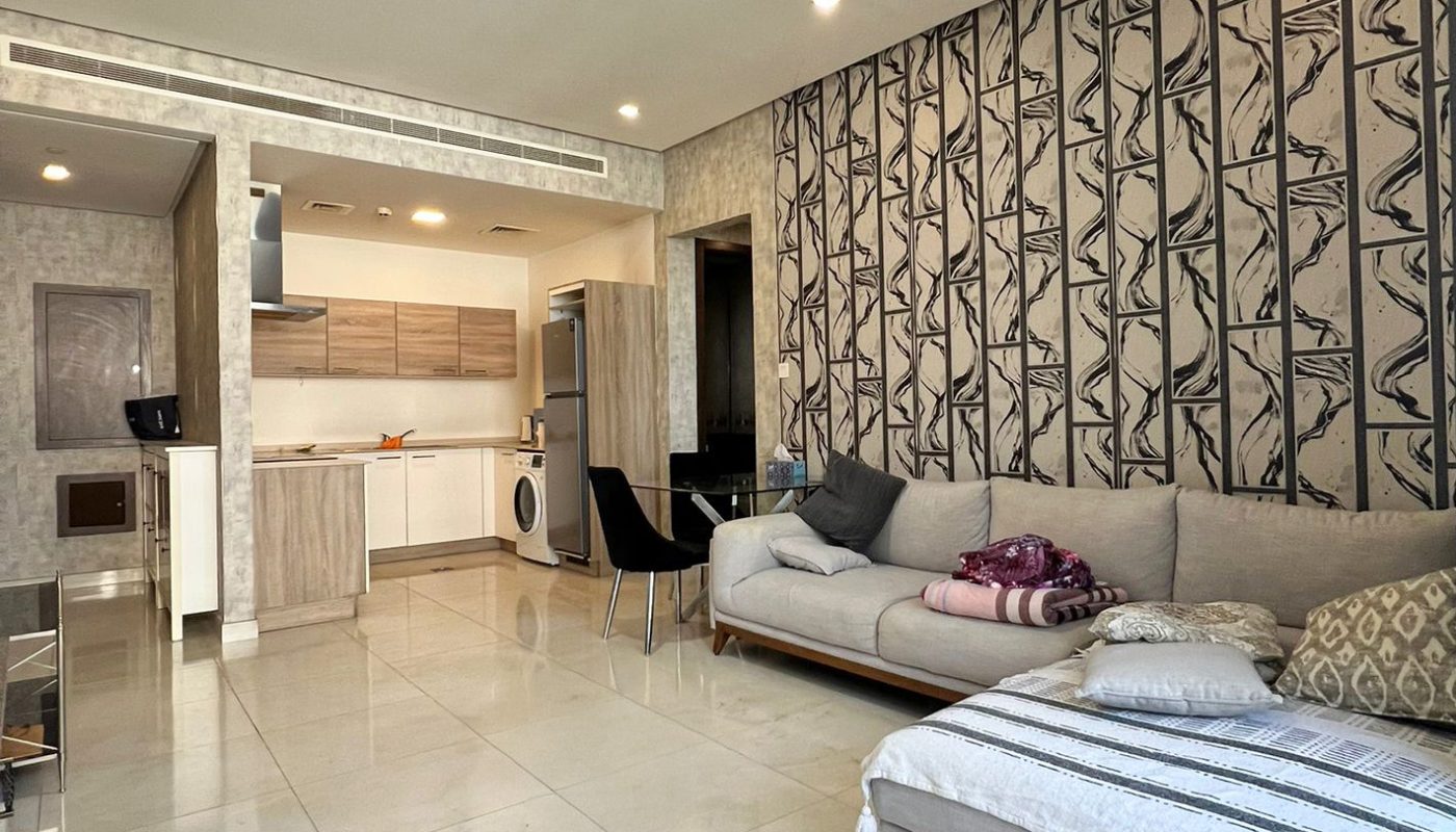 Modern open-plan living room and kitchen with tiled flooring, patterned accent wall, grey sofa, daybed, and minimalist furniture.