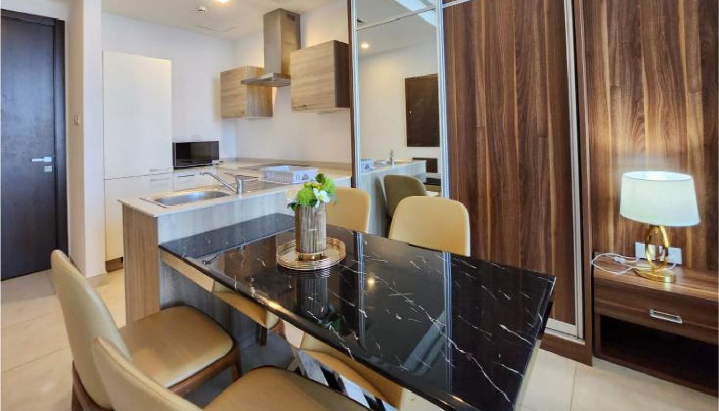 Modern dining and kitchen area with a black marble table, beige chairs, wood cabinets, and a lamp on a side table in a well-lit apartment.