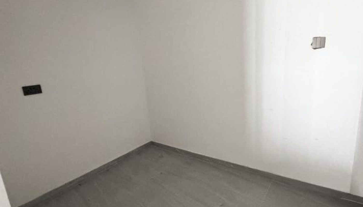 A small, empty room with white walls, gray tiled floor, and a partial view of an unfinished ceiling with exposed ductwork.