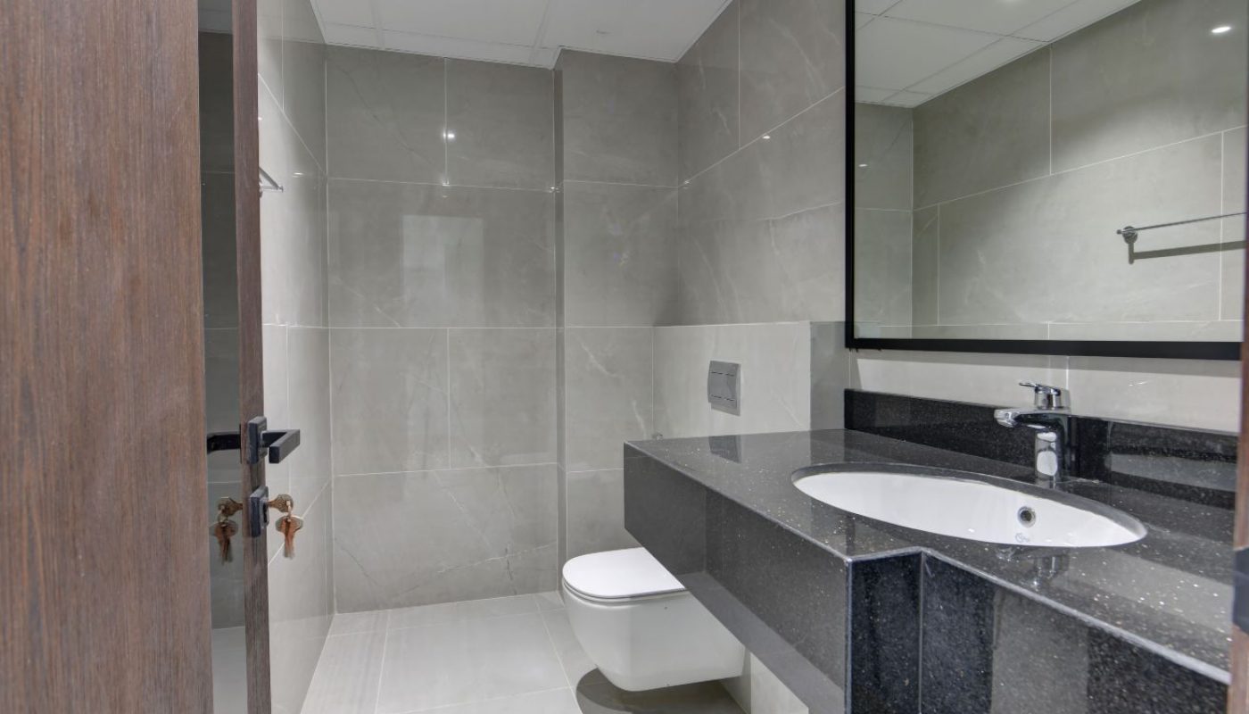 Modern bathroom with gray tiled walls, a wall-mounted toilet, a black countertop with a white sink, and a large mirror above the sink.