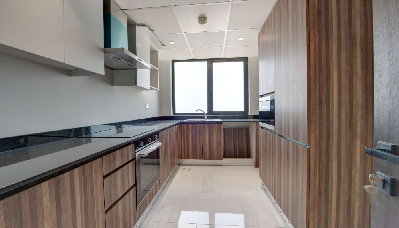 Modern kitchen with wood-paneled cabinets, black countertops, built-in oven, gas stove, and a large window providing natural light.