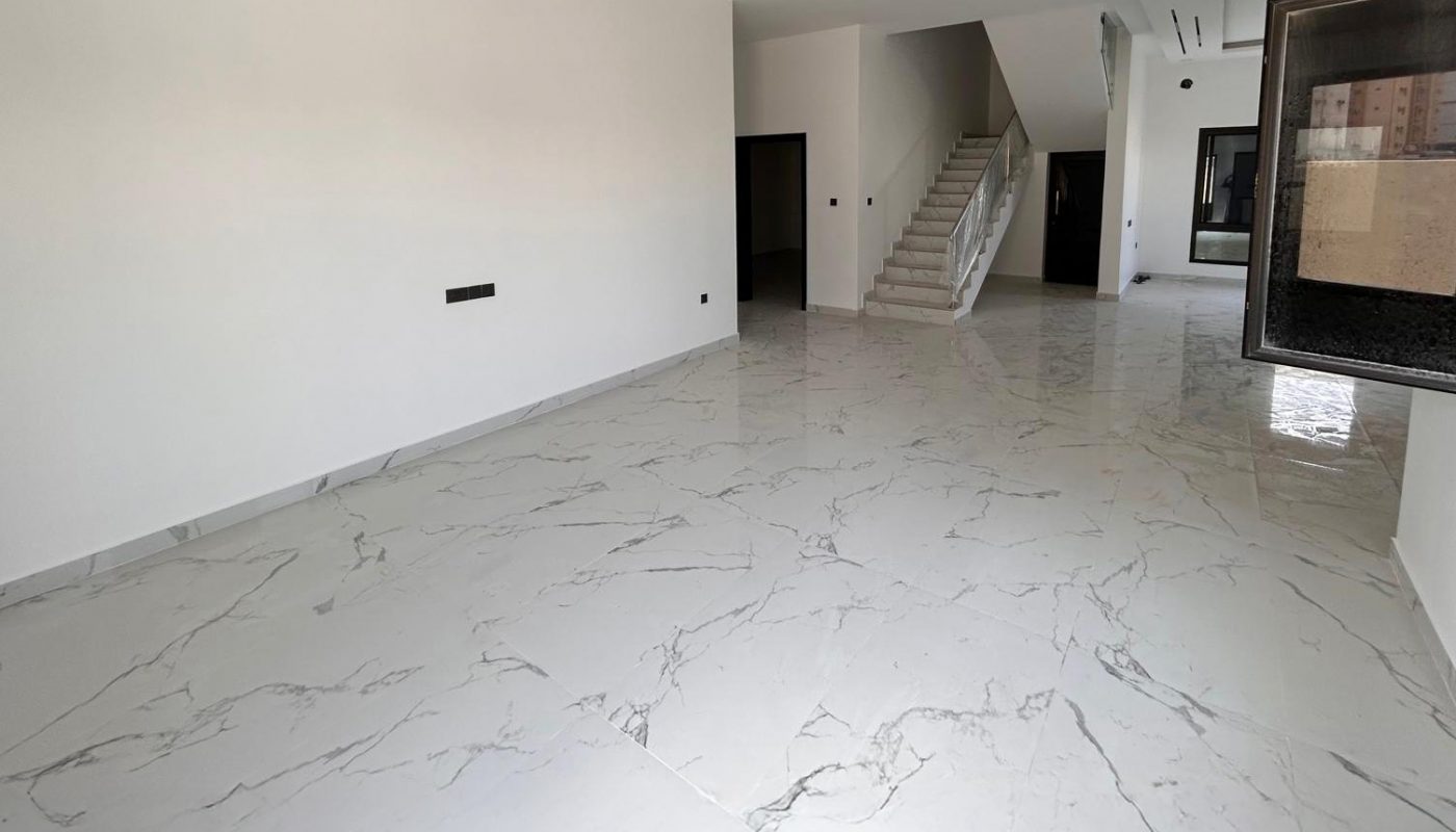 Spacious, empty room with white marble floors, white walls, recessed lighting, a staircase, and large windows.
