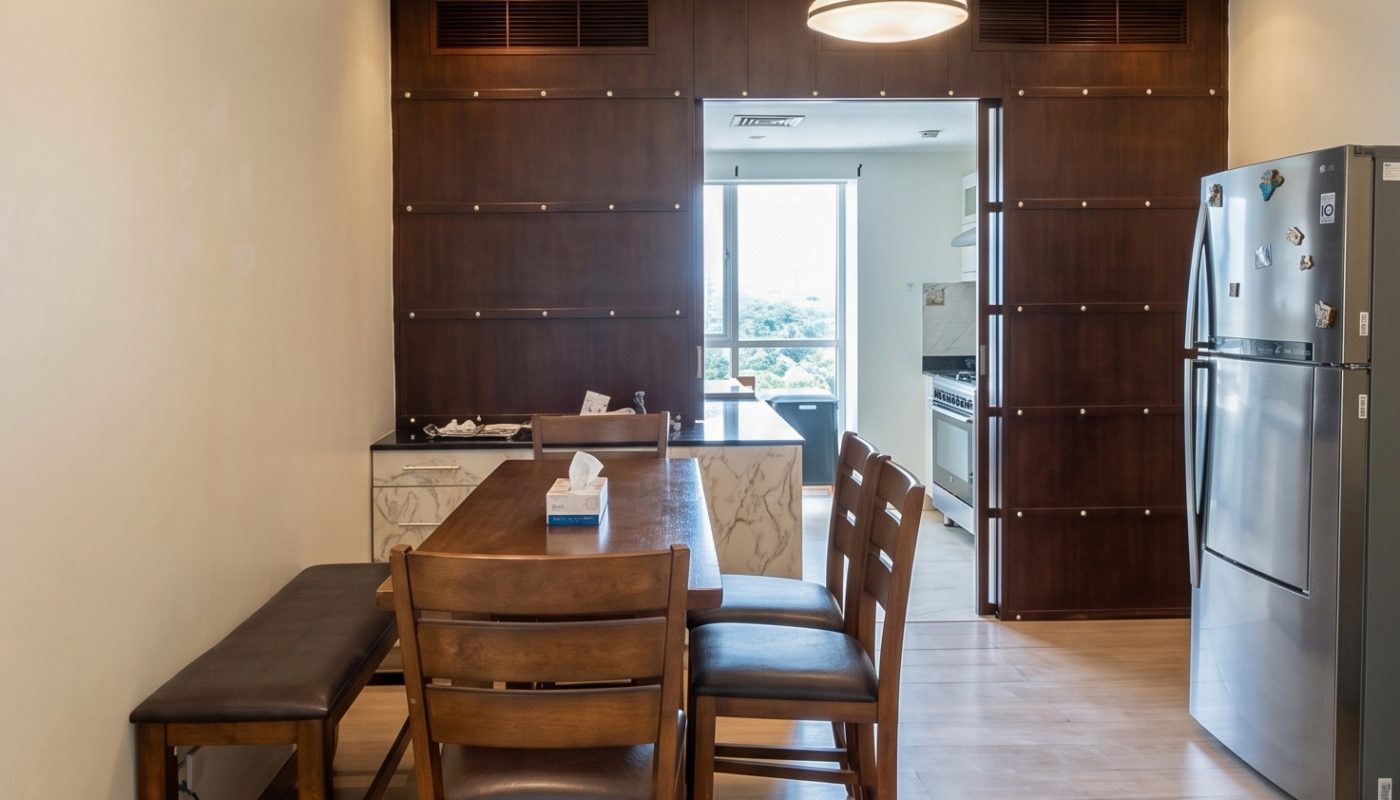 Modern dining area with a wooden table, chairs, and bench, adjacent to a kitchen with stainless steel refrigerator and a window in the background.
