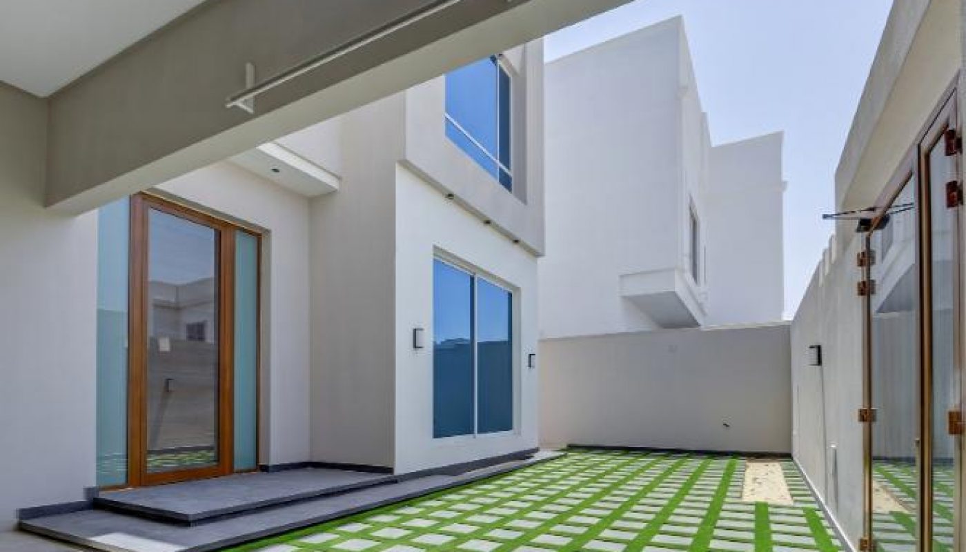 Modern courtyard with a grid pattern of grass and stone, surrounded by white walls, large windows, and glass doors.