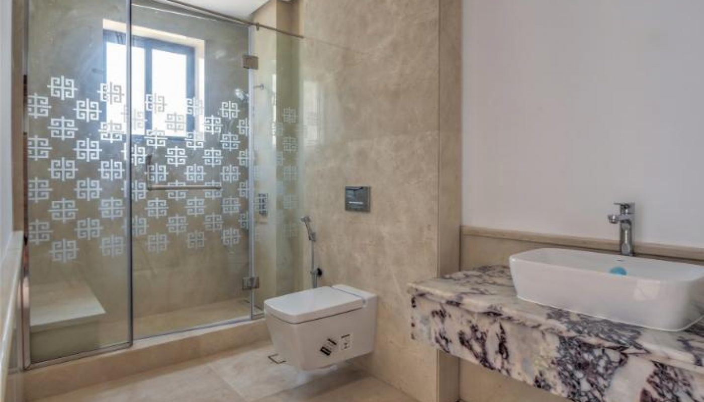 Modern bathroom with marble floors, wall-mounted toilet, glass shower enclosure with patterned glass, and a marble countertop with a white vessel sink.