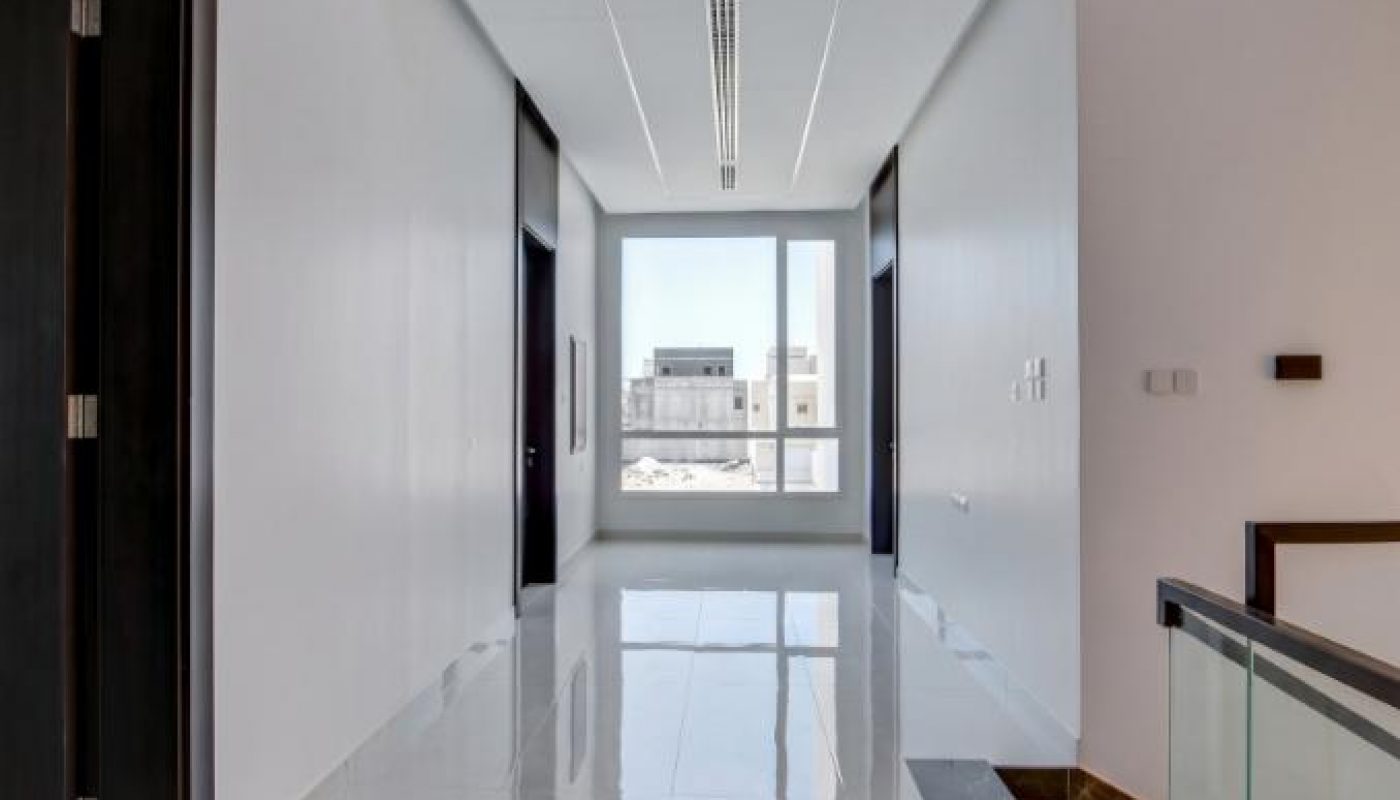 A modern, bright hallway with white walls, glossy marble floor, dark door frames, and a large window at the end letting in natural light.