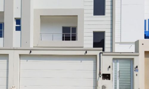 A luxury white villa with two garages in the middle of the sand.