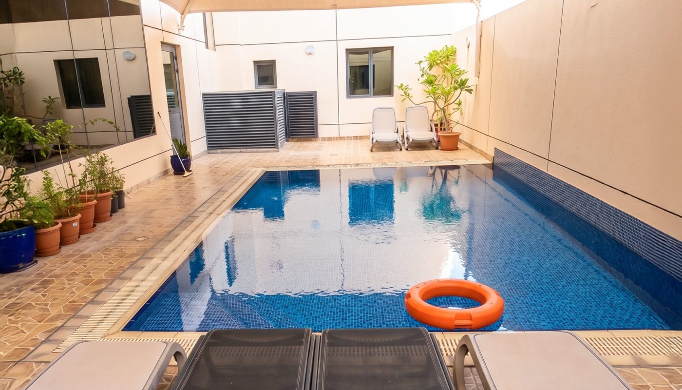 Small private outdoor pool with blue tiles, two poolside lounge chairs, potted plants, a shade canopy overhead, and an orange life ring floating in the water.