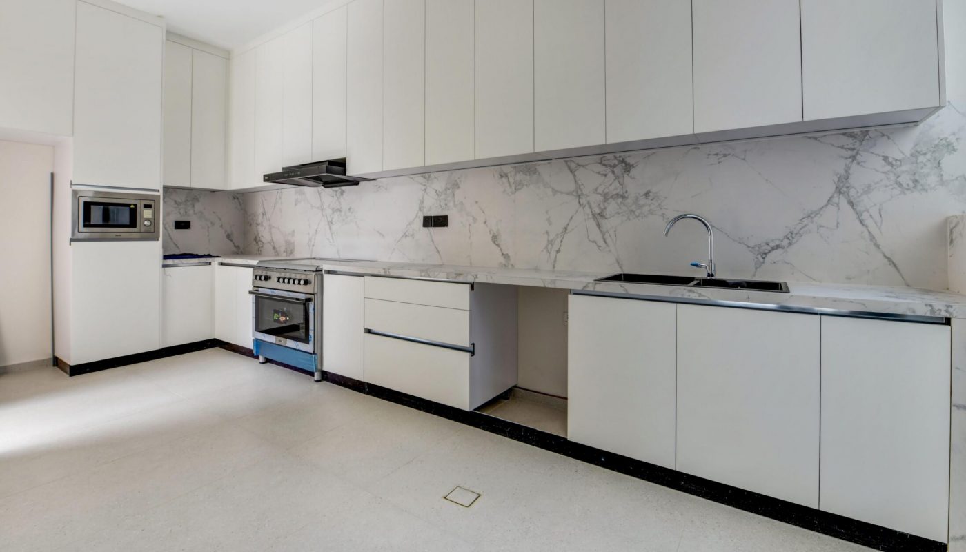Modern kitchen with white cabinets, marble backsplash, built-in microwave, stove, and sink, featuring minimalistic design and ample counter space.