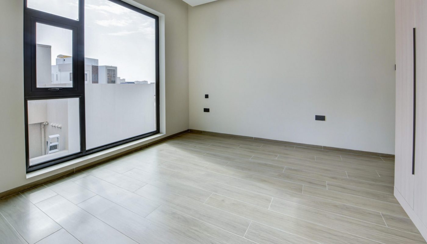 Empty room with light wood flooring, large window, beige walls, and minimal ceiling light fixture. Built-in closet is visible on the right side.