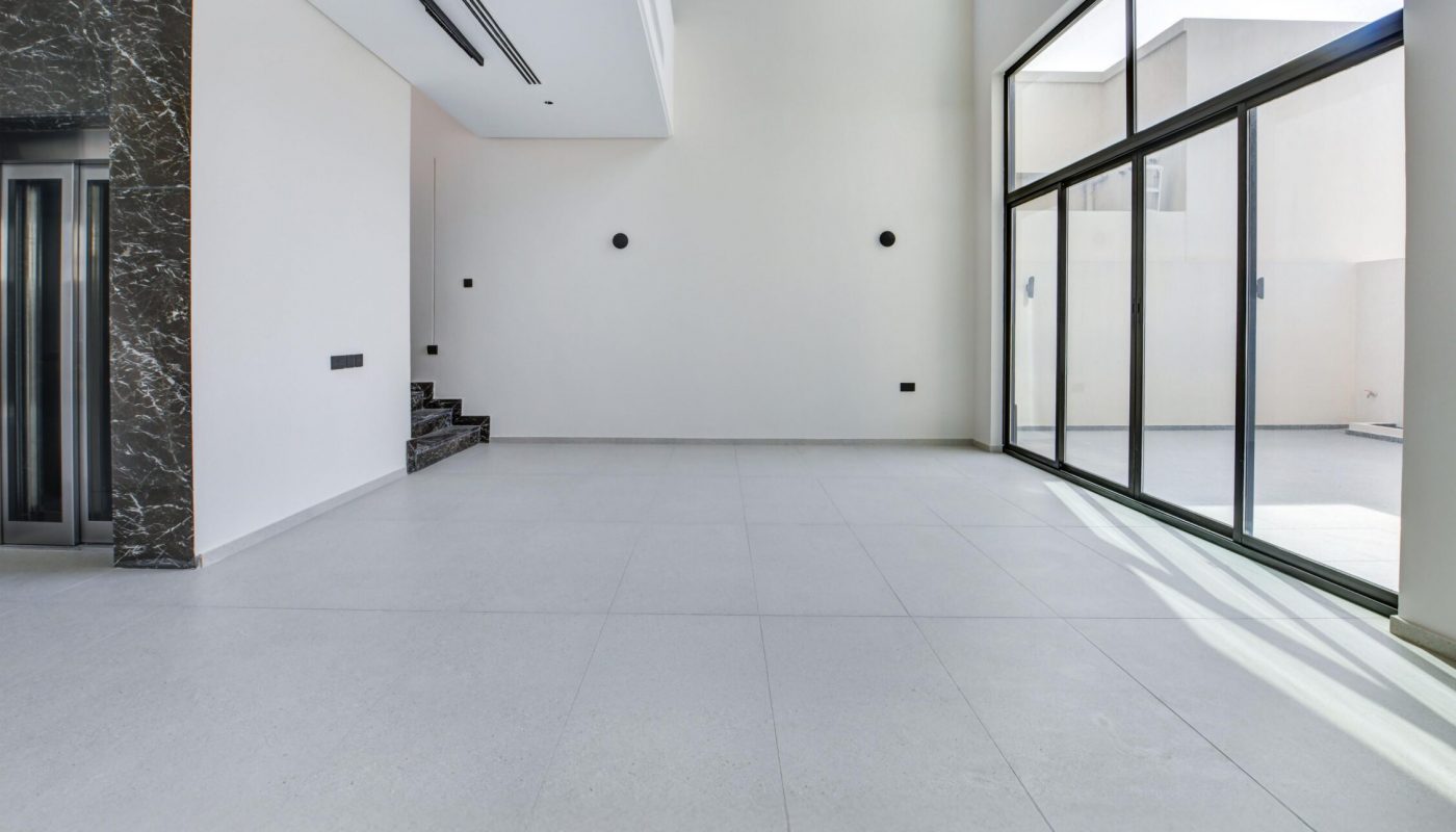 Spacious, unfurnished modern room with large windows, white walls, tiled floor, and an elevator next to dark marble wall panels.
