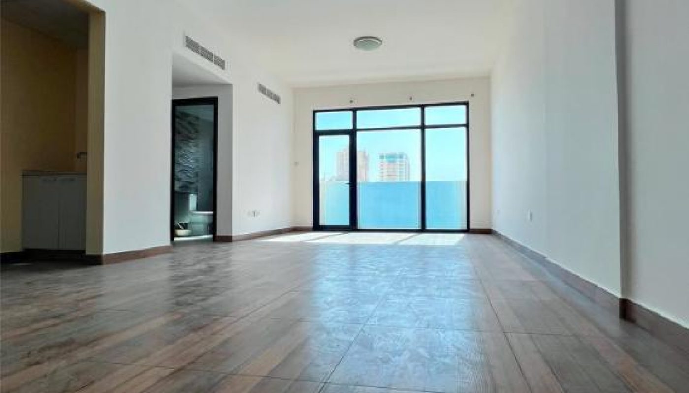 Empty room with wood flooring, white walls, large window with glass door, and ceiling lights; view faces the window and balcony.