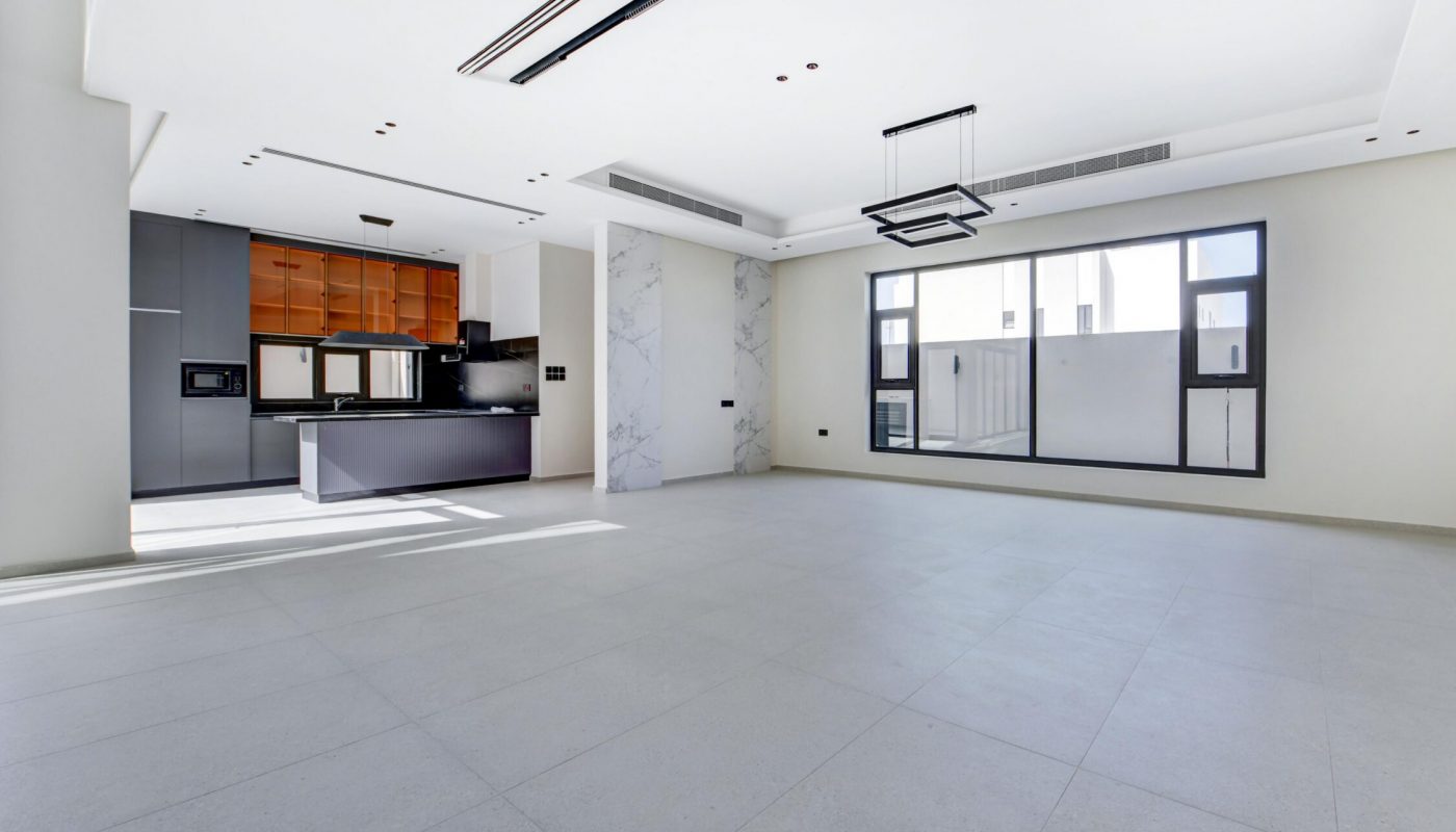 Spacious, unfurnished modern living area with large windows, tiled flooring, and a visible open kitchen featuring wood and gray cabinetry.