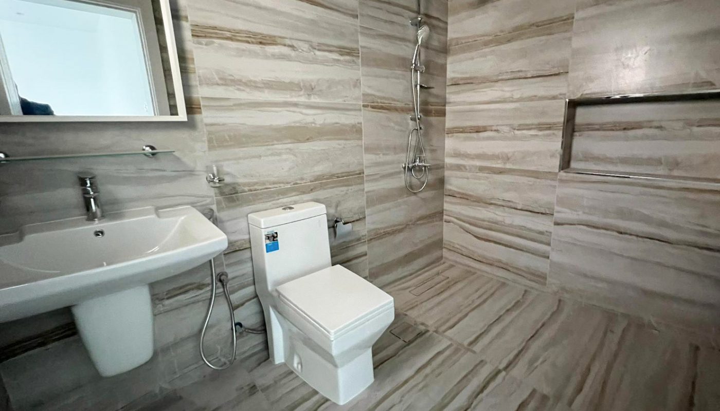 Bathroom with marble-patterned walls and floor, featuring a wall-mounted sink, toilet, and a shower area with a rain showerhead.