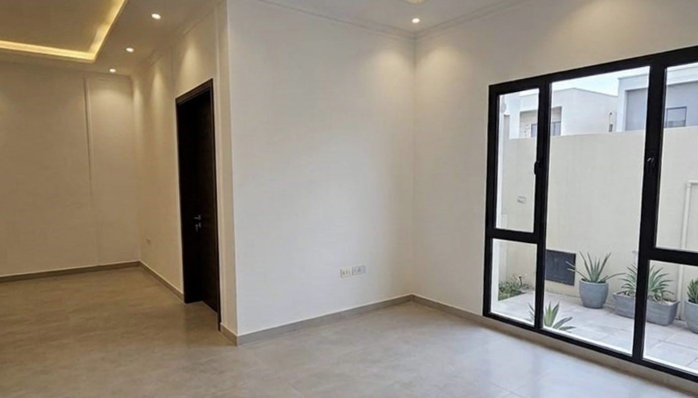 A modern, empty room with large windows, recessed ceiling lights, light grey floor tiles, and white walls.