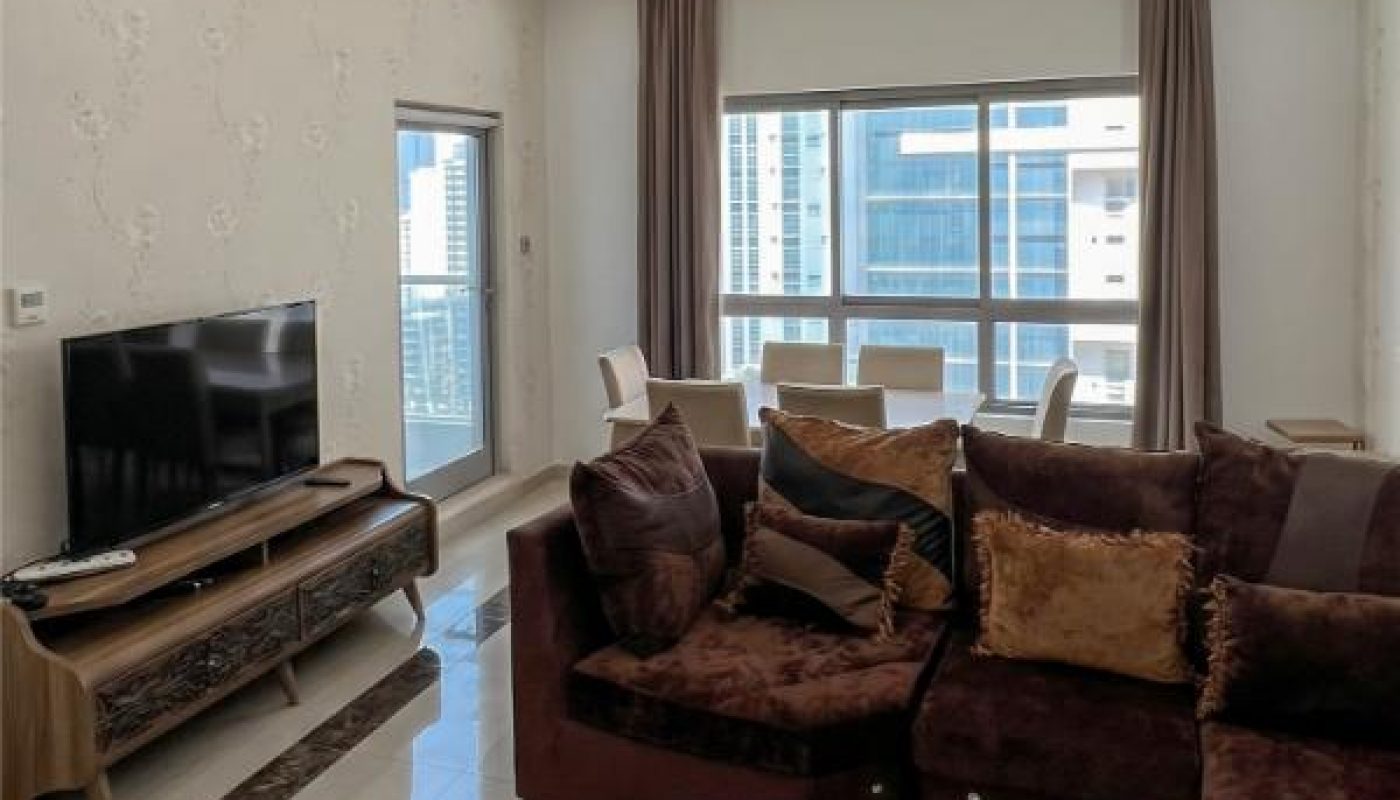 Modern living room with a brown sectional sofa, marble coffee table, flat-screen TV on a console, and large windows with city views and natural light.