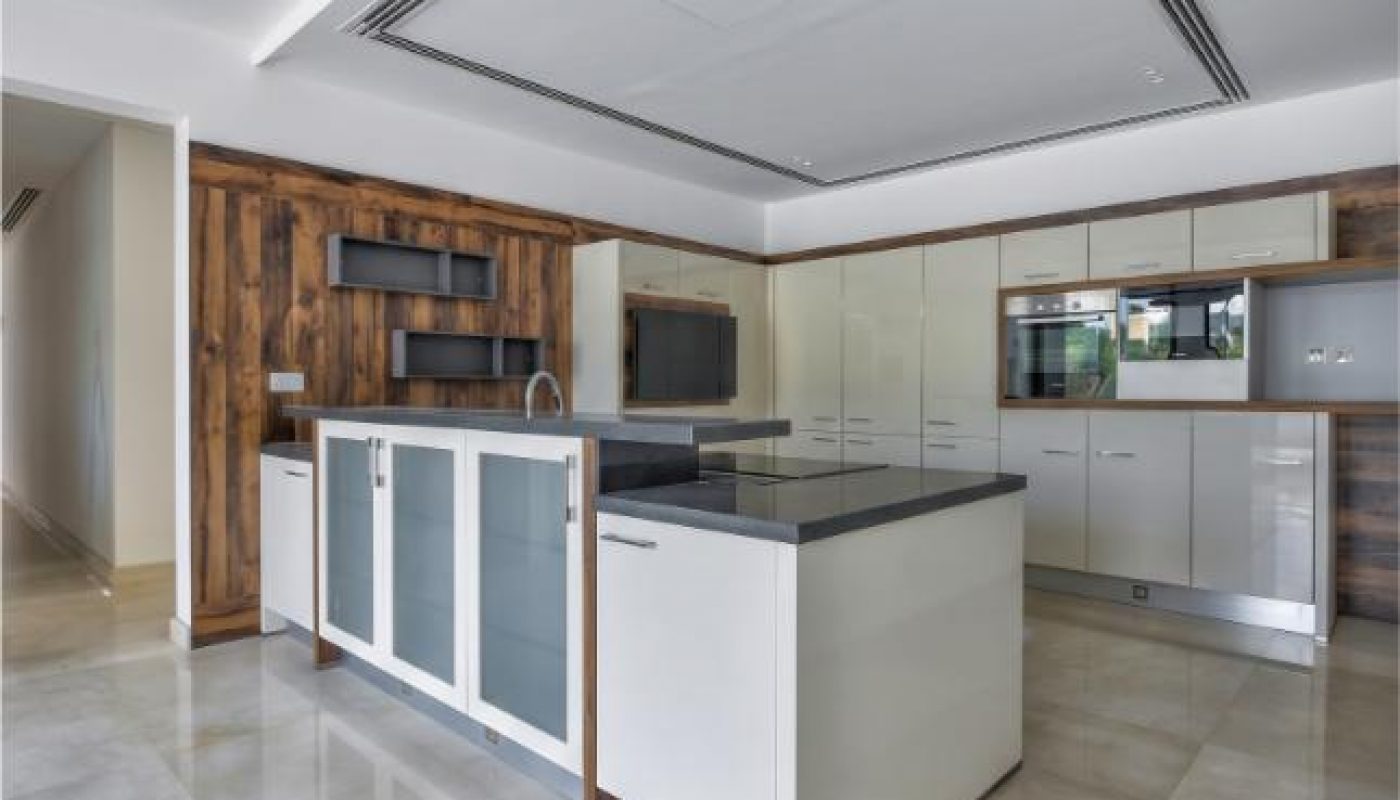 Modern kitchen with a large island, white cabinets, wooden accents, built-in appliances, and glossy marble flooring.